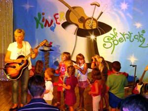 Karin Meier abends mit
Gitarre und einigen Kindern auf der Kinderspektakel-Bühne.
