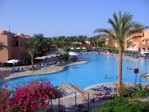 Ein Swimming Pool, umsäumt
von Palmen und Wohnungen der Hotelanlage.