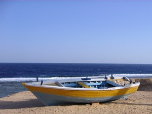 Ein Ruderboot liegt auf dem
Sandstrand, dahinter das tiefblaue Meer und darüber der hellblaue
Himmel.