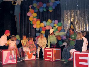 Karin mit Kollegen und den Kindern auf der Bühne. Im Hintergrund viele Luftballons.