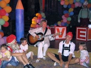Karin spielt Gitarre im Kreis der Kinder vor der Bühne.